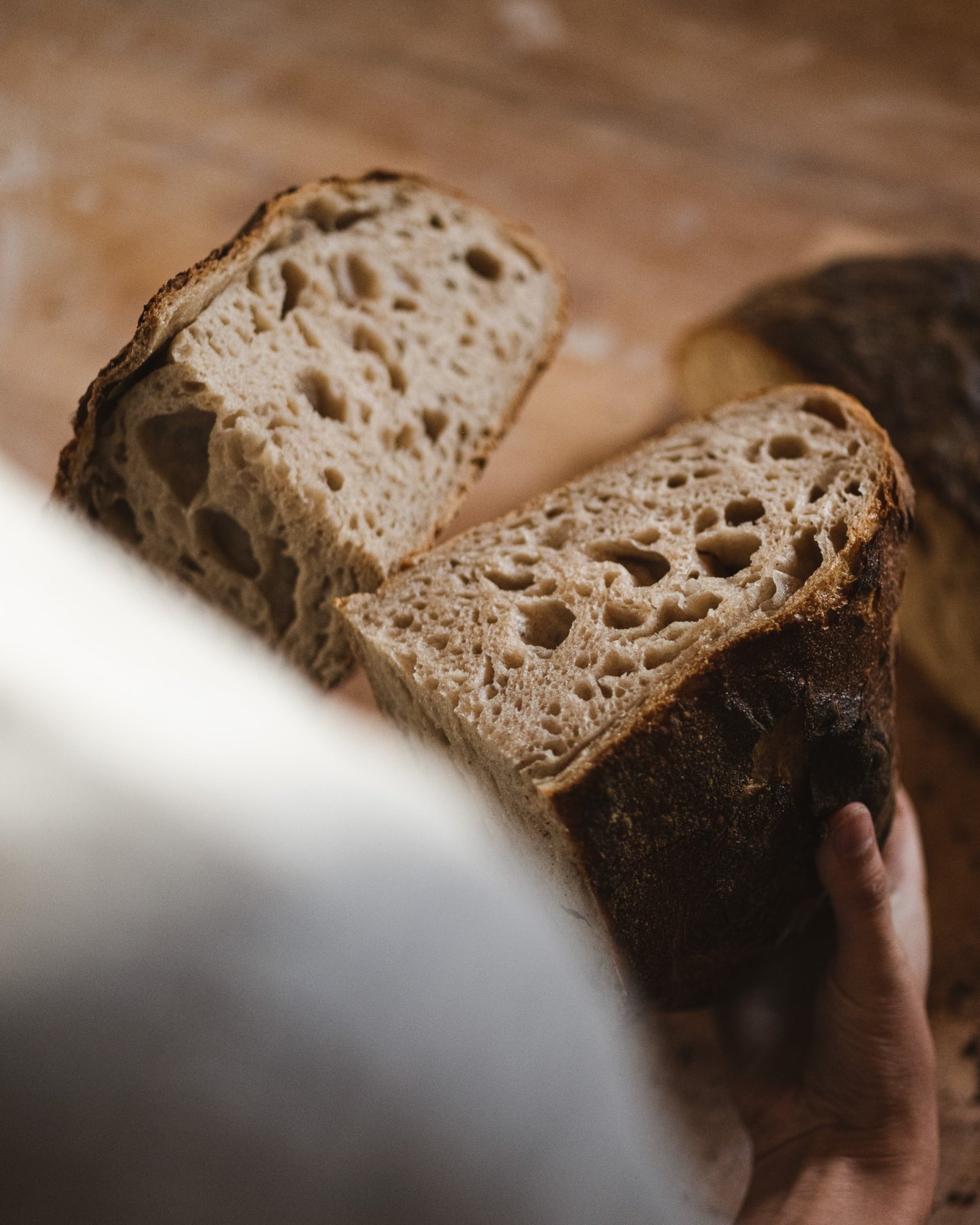 Eine Person hält ein aufgeschnittenes Brot mit einer dicken Kruste und einer luftigen, porigen Krume. Die Schnittfläche zeigt große Löcher.